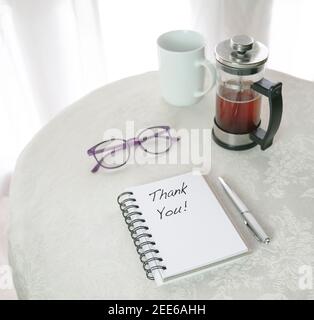 Merci, les mots écrits sur le bloc-notes, à côté de French Press avec café, tasse et lunettes sur la table blanche. Banque D'Images