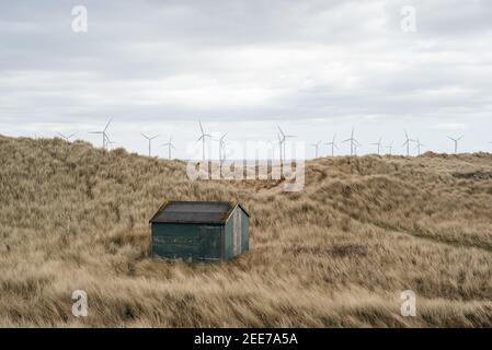 Cabane de pêcheurs de couleur verte à South Gare, Redcar, Angleterre, près de Paddy's Hole, avec parc d'éoliennes Teeside en arrière-plan au large. Banque D'Images