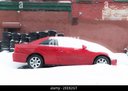 Voiture rouge recouverte de neige avec des pneus en arrière-plan sur la rue City. Sensation de neige et de circulation. Idées de travail à domicile et de télétravail. Banque D'Images