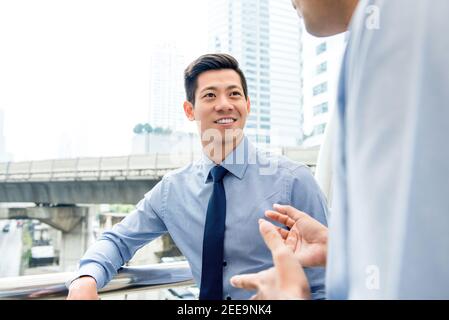 Beau homme d'affaires asiatique chinois parlant avec un collègue en plein air dans le ville Banque D'Images