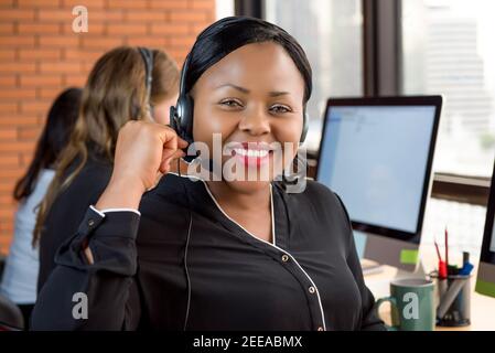 Belle femme d'affaires noire souriante travaillant dans le centre d'appels comme un agent du service à la clientèle avec son équipe multiethnique Banque D'Images