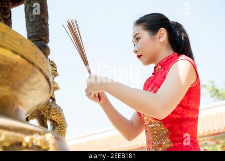 Femme asiatique en rouge qipao robe priant avec des bâtons d'encens Durant la nouvelle année chinoise ou lunaire Banque D'Images