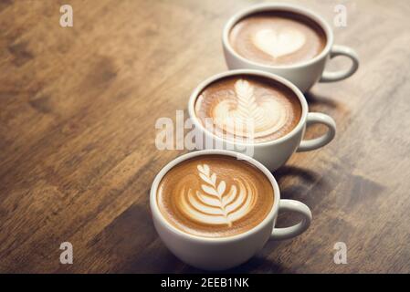 Cafés fraîchement préparés avec de beaux latte en surface, trois tasses d'affilée sur une table en bois prête à boire Banque D'Images