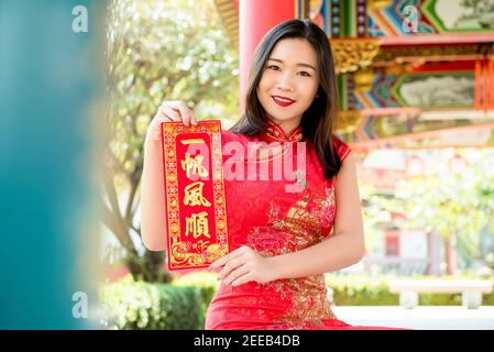 Femme asiatique souriante dans le cheongsam rouge traditionnel qipao robe montrant Signe de texte de salutation du nouvel an chinois dit "tout sera bon' Banque D'Images