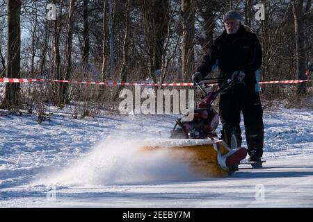 L'homme nettoie la patinoire dans la neige d'hiver avec un balai et un souffleur de neige. Il peut être tiré sur un traîneau. Banque D'Images