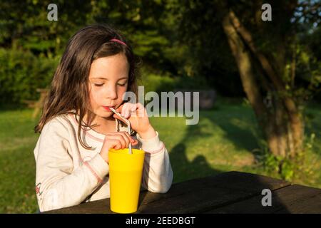 Petite fille buvant d'un bécher jaune à travers une paille en plastique à une table de pique-nique, Kent Banque D'Images