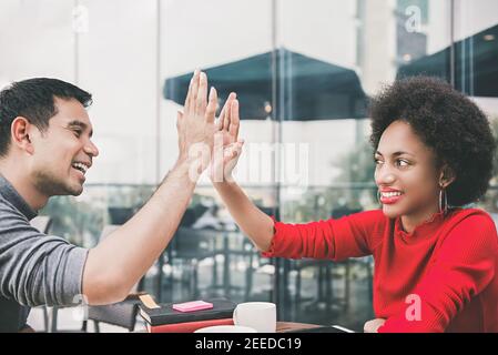 Amis interraciaux, homme asiatique et femme noire, faisant cinq hauts célébrer après une réunion d'affaires dans un café-restaurant Banque D'Images