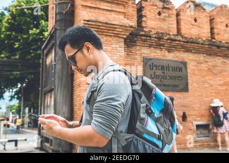 Asian man touriste routard à l'aide d'un smartphone à la recherche d'informations tout en voyageant à Chiang Mai Thaïlande. Panneau sur le mur dit THA PHAE PORTE Banque D'Images