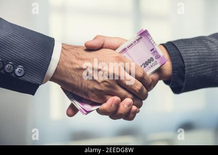 Les hommes d'affaires font la poignée de main avec de l'argent, monnaie de roupie indienne, entre les mains - corruption concept Banque D'Images