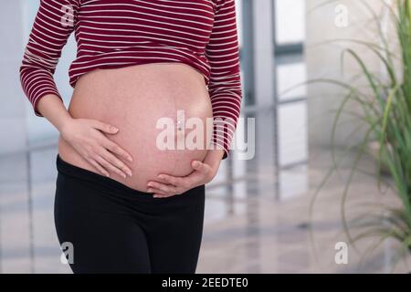 Jeune enceinte jeune femme enceinte marchant et tenant son ventre sur un fond flou. Mise au point sélective. Banque D'Images