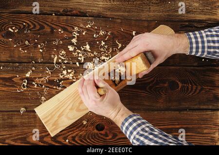 carpenter plane une pièce sur un établi. vue de dessus. mains de carpenter. ancien plan en bois Banque D'Images