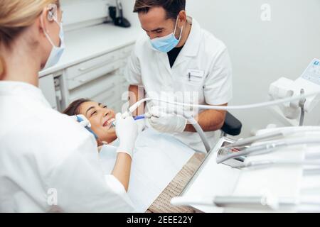 Dentiste et son assistant examinant les dents d'une patiente. Femme qui reçoit un traitement dentaire en clinique. Banque D'Images