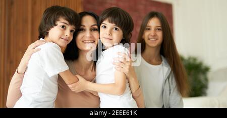 Portrait d'enfants latins mignons, petits garçons jumeaux regardant l'appareil photo et embrassant leur mère, passant du temps ensemble à la maison. Mère et enfants se posant ensemble à l'intérieur. Famille, concept d'enfance Banque D'Images