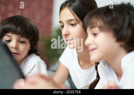 Gros plan de la jeune fille latine avec une tablette numérique. Soeur passant du temps avec ses deux petits frères, allongé sur le lit à la maison. Bonne enfance, concept de technologie Banque D'Images