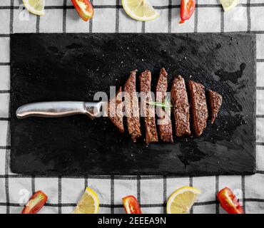 Steak de bœuf grillé, filet de bœuf sur une assiette de pierre noire avec tomates et citron Banque D'Images