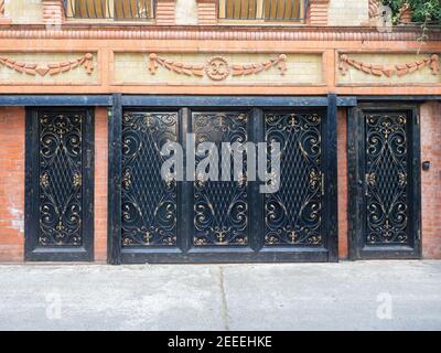 Portes et portails de garage en fer noir à motif doré de monogrammes et de barres dans une maison en brique avec ornement maçonnerie Banque D'Images