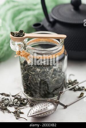 Pot en verre de thé vert en vrac biologique avec infuser de crépine en métal vintage sur fond clair avec théière en fer japonais et chiffon vert. Banque D'Images