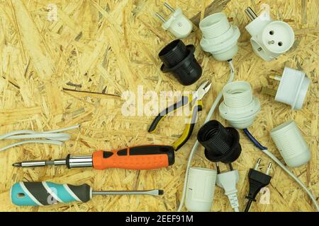 Les tournevis et les outils électriques sont répartis sur la table. Outils d'électricien sur une table en bois. Les tournevis, les cartouches, les fiches, les fils sont posés ou Banque D'Images