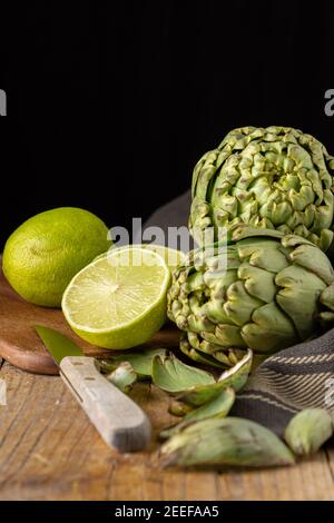 Vue de dessus d'artichauts verts avec tissu noir, limes sur la table et le couteau, sur la table en bois, avec mise au point sélective, fond noir, à la verticale, avec co Banque D'Images