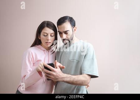 Deux hommes et femmes adultes étant surpris choqué regarder l'écran du téléphone. Achats en ligne, s'amuser. Porter un pull à capuche décontracté rose pastel. Vide Banque D'Images