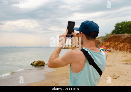 Homme attrapant le signal sur la plage sauvage, en faisant la photo de paysage marin. Arrière wiew Banque D'Images