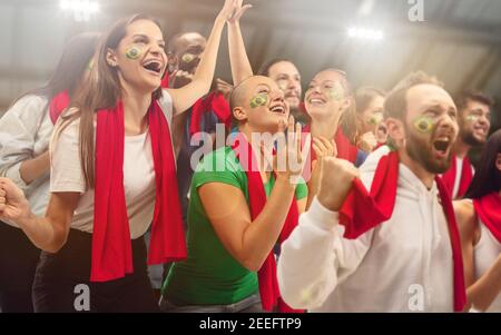 Le football brésilien, les fans de football applaudissent leur équipe avec des foulards rouges au stade. Les fans enthousiastes applaudissent un but, soutenant les joueurs favoris. Concept de sport, émotions humaines, divertissement. Banque D'Images