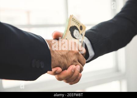 Homme d'affaires faisant la poignée de main avec de l'argent, la Corée du Sud a gagné des billets, en mains - concept de corruption Banque D'Images
