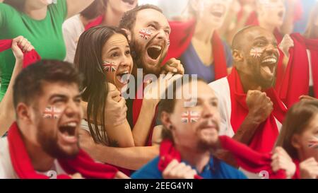 Le football britannique, les fans de football applaudissent leur équipe avec des foulards rouges au stade. Les fans enthousiastes applaudissent un but, soutenant les joueurs favoris. Concept de sport, émotions humaines, divertissement. Banque D'Images