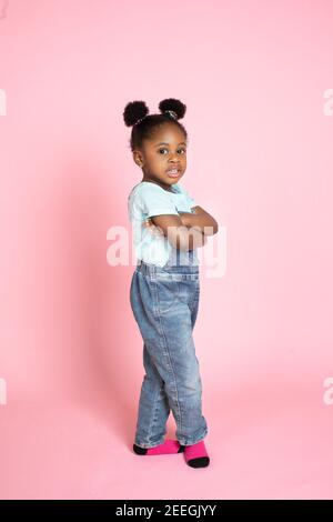 Concept de bonheur, d'enfants, d'émotions. Plein studio de photo adorable petite fille africaine, portant des combinaisons de jeans stylées, posant à l'appareil photo Banque D'Images