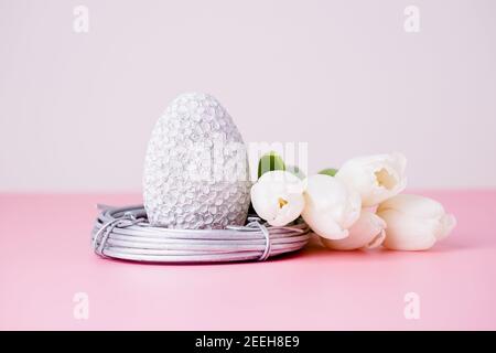 Oeuf de pâques argenté dans le nid et tulipes blanches sur un fond rose Banque D'Images