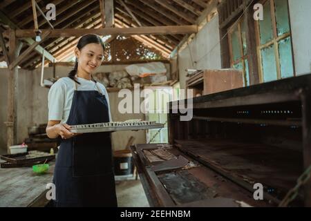 la fille dans un tablier porte une plaque de cuisson de pâte à gâteau à mettre dans le four déjà éclairé avec la cuisine en arrière-plan Banque D'Images