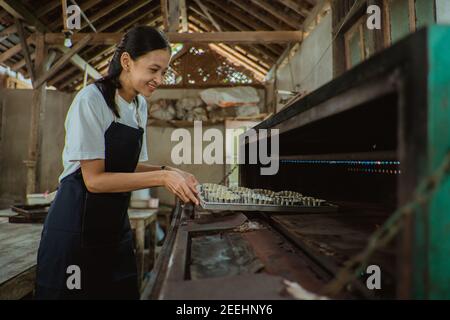 femme souriante portant un tablier qui lance la casserole de gâteau batter dans le four avec la cuisine comme arrière-plan Banque D'Images