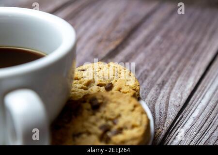 biscuits aux pépites de chocolat à côté d'une tasse de café une soucoupe sur une table rustique en bois Banque D'Images