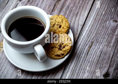 biscuits aux pépites de chocolat à côté d'une tasse de café une soucoupe sur une table rustique en bois Banque D'Images