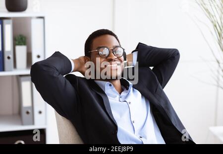 Joyeux homme d'affaires noir couché sur une chaise dans son cabinet Banque D'Images