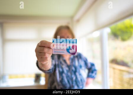 Elle tient sa carte de vaccination NHS Covid-19. Banque D'Images