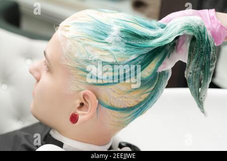 Laver la couleur des cheveux émeraude de la jeune femme avec du shampooing dans l'évier. Coiffeur professionnel avec gants de protection roses dans un salon de coiffure professionnel. Banque D'Images
