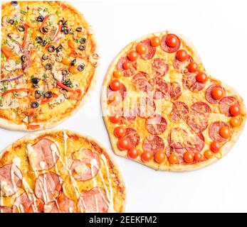 trois différentes sortes de pizzas, autour et coeur en forme de fond blanc avec espace de copie, salami, champignons, tomaton, pepperoni, tomates cerises et Banque D'Images