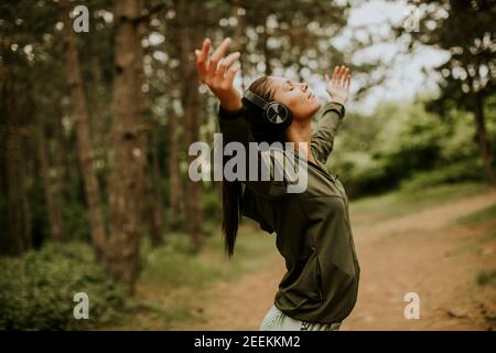 Jolie jeune femme avec des écouteurs qui la préécoute dans les bras de la forêt parce qu'elle aime l'entraînement à l'extérieur Banque D'Images