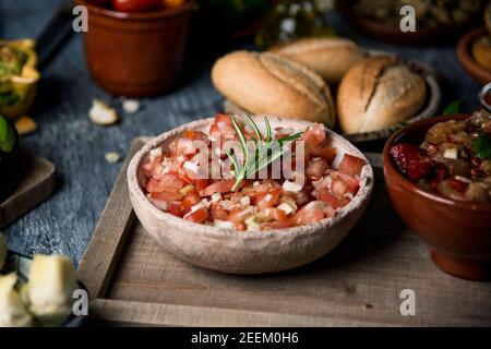 gros plan d'une salade de tomates servie dans un bol rustique sur une table rustique grise à côté de quelques assiettes et bols avec autres ingrédients végétariens et accompagnement Banque D'Images