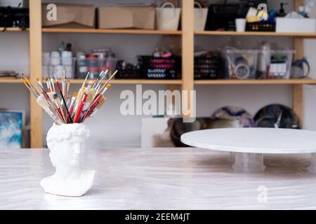 Atelier de travail de l'artiste. Vase en plâtre, support, brosses, peintures, toile ronde pour la peinture, étagères. Concept d'artiste. Banque D'Images