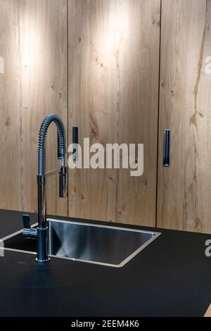 Évier et robinet en acier inoxydable fixés sur des surfaces noires en pierres naturelles. Cuisine en bois beige armoire arrière-plan Banque D'Images