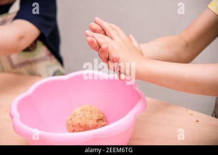 Fille enfant sculpte de la pâte, la créativité avec la pâte. Petites mains pour enfants gros plan, bol rose avec pâte sur table. Banque D'Images