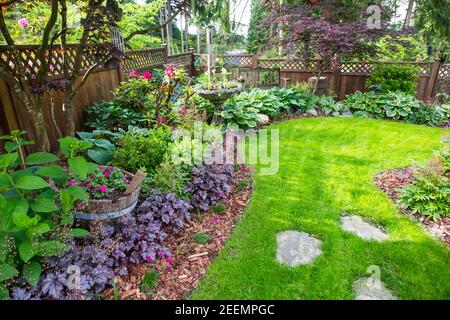 Chemin menant à un magnifique jardin arrière plein de plantes, vivaces et annuelles le jour du printemps. Banque D'Images