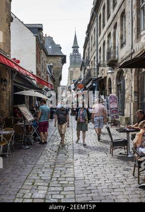 Les gens se baladent le long d'une rue pavée sous un soleil brumeux, les cafés en plein air dans le vieux quartier de Dinan, en France, portant des masques faciaux en raison de la pandémie Banque D'Images