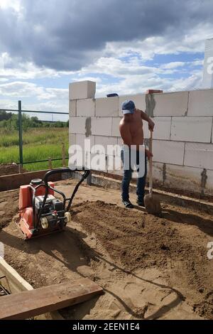 Plaque vibrante en cours d'utilisation, le travailleur à l'aide d'une plaque vibrante compacte le sable, construisant une maison.New Banque D'Images