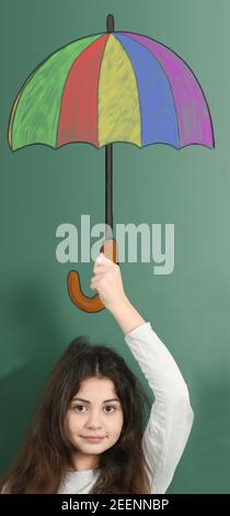 Enfant préadolescent portant un parapluie peint de couleur sur un fond vert. Banque D'Images