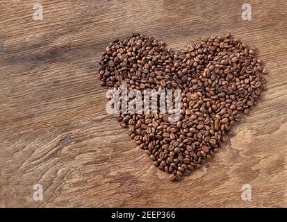 Forme de coeur faite d'un tas de grains de café sur une texture en bois avec un fond pour la Saint Valentin. Symbole de l'amour au café, foyer sélectif. Banque D'Images
