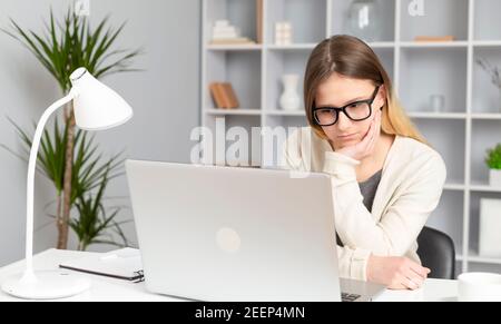 Une jeune fille élève écoute attentivement une leçon en ligne à l'aide d'un ordinateur portable. Une jeune femme regarde l'écran d'ordinateur avec concentration. Banque D'Images