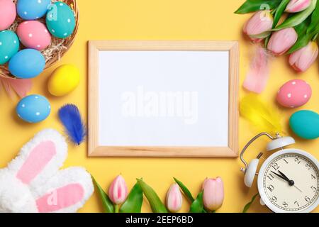 Joyeuses Pâques. Œufs multicolores, tulipes et réveil sur fond jaune. Carte de vœux d'invitation à poser à plat avec espace de copie. Banque D'Images